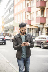 Young businessman using smart phone while walking on sidewalk in city - MASF17492