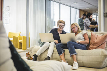 Full length of female entrepreneurs working over laptop while sitting on sofa in office - MASF17496