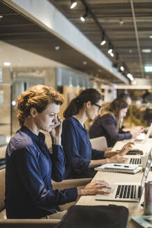 Geschäftsfrau arbeitet an einem Laptop, während sie mit Kollegen in einem kreativen Büro sitzt - MASF17508