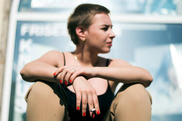 Junge Frau schaut weg, während sie im Freien sitzt - EYF02619