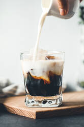 Close-Up Of Hand Pouring Milk In Coffee Cup On Table - EYF02920