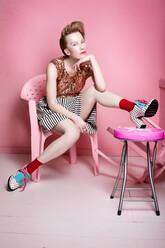 Porträt einer Frau, die auf einem Stuhl vor einer rosa Wand sitzt - EYF02923