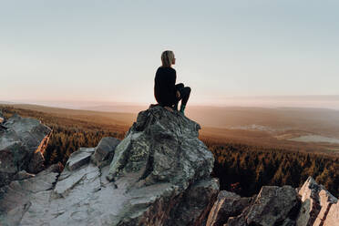 Frau auf einem Felsen sitzend vor Landschaft - EYF02933