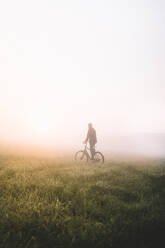 Volle Länge des Mannes mit Fahrrad auf dem Feld bei nebligem Wetter - EYF03023