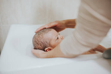 Nahaufnahme des Vaters, der ein Baby in der Badewanne im Badezimmer hält - EYF03034
