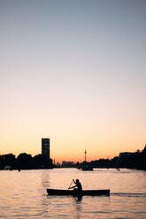 Silhouette Mann auf Boot in Fluss von Stadt gegen klaren Himmel - EYF03138