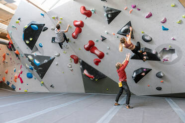 Männlicher Trainer trainiert Frau und Mann im Klettern an der Wand in einem Fitnessstudio - MASF17522