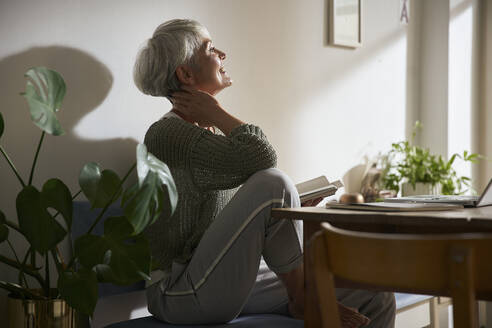 Selbstbewusste ältere Frau mit Notebook und Laptop, die sich zu Hause entspannt - AUF00290
