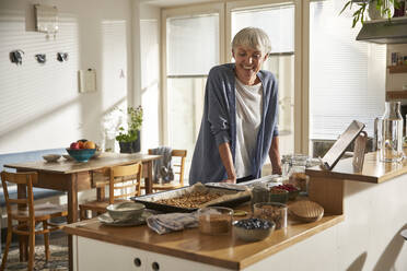 Porträt einer lächelnden älteren Frau, die in der Küche steht und Müsli zubereitet - AUF00306
