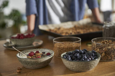 Bowl of granola with yoghurt and berries and bowls of ingredients on kitchen counter - AUF00313