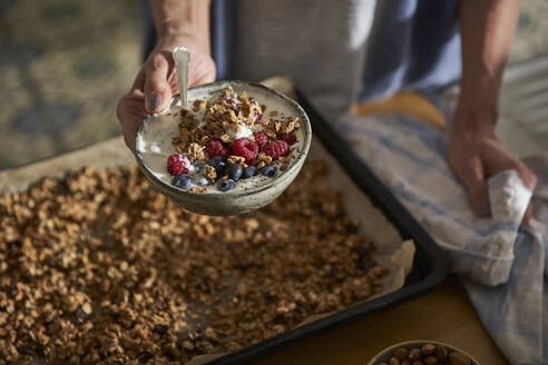 Woman's hand holding bowl of granola with yoghurt and berries - AUF00315