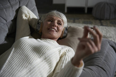 Portrait of senior woman relaxing on couch listening music with headphones - AUF00319