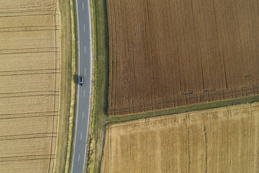 Deutschland, Bayern, Drohnenansicht einer Landstraße, die durch braune und gelbe Felder im Sommer führt - RUEF02717