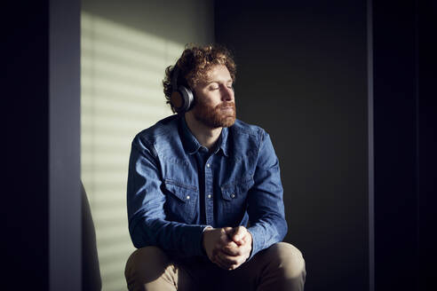 Relaxed casual businessman sitting down listening to music with headphones - RBF07233