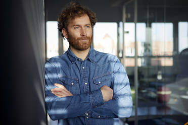 Portrait of a casual businessman leaning against a wall in office - RBF07247