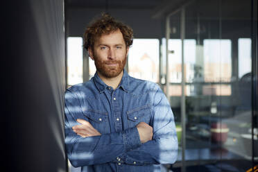 Portrait of a casual businessman leaning against a wall in office - RBF07248