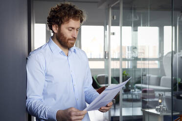 Portrait of a businessman reading papers in office - RBF07261