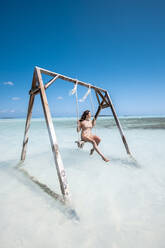 Woman swinging on swing in the sea, Bahamas, Caribbean - DAWF01327