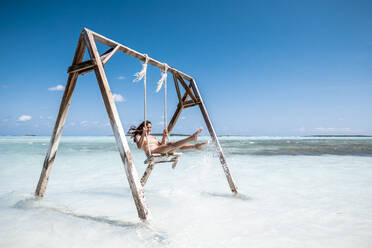 Frau schwingt auf einer Schaukel im Meer, Bahamas, Karibik - DAWF01328