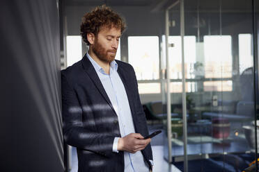 Businessman using cell phone in office - RBF07302