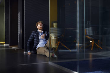 Businessman sittting on the floor in office with closed eyes - RBF07306