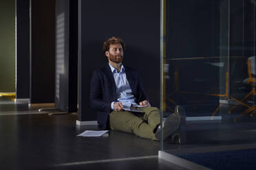 Businessman sittting on the floor in office with closed eyes - RBF07308