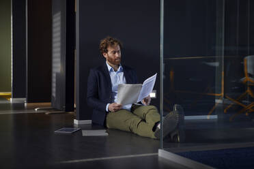 Geschäftsmann sitzt auf dem Boden im Büro und liest Zeitung - RBF07309