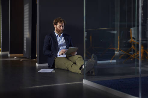 Geschäftsmann sitzt auf dem Boden im Büro und benutzt ein Tablet - RBF07310