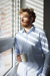 Porträt eines Geschäftsmannes, der eine Kaffeetasse hält und aus dem Fenster schaut - RBF07311