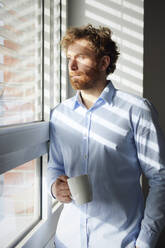 Portrait of businessman holding coffee mug looking out of window - RBF07311