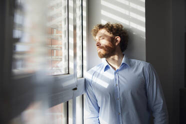 Portrait of businessman at the window with closed eyes - RBF07312