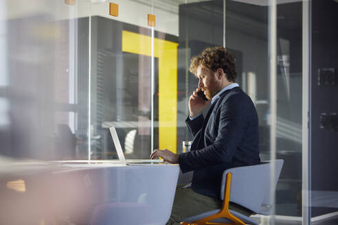 Geschäftsmann sitzt am Schreibtisch im Büro und benutzt Laptop und Smartphone - RBF07317