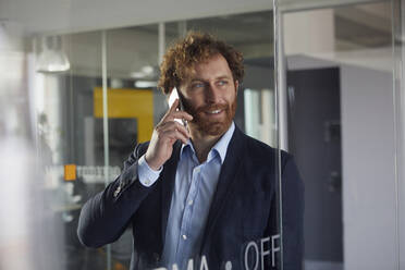 Portrait of smiling businessman in office on the phone - RBF07319