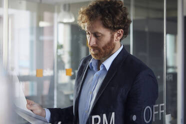 Portrait of businessman reading papers in office - RBF07322