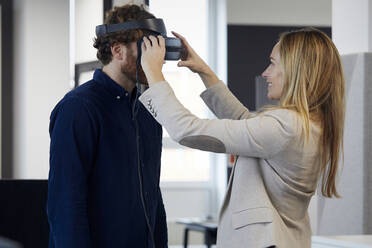 Businesswoman applying VR glasses on businessman in office - RBF07326