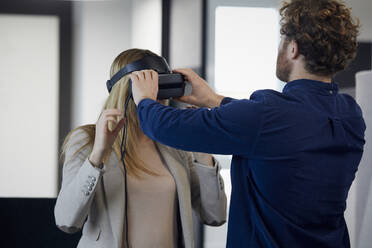 Geschäftsmann setzt VR-Brille auf Geschäftsfrau im Büro auf - RBF07331