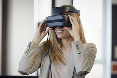 Smiling businesswoman wearing VR glasses in office - RBF07332