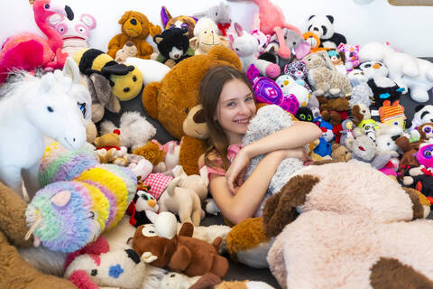 Girl sitting on couch, covered in cuddly toys stock photo
