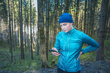 Young female jogger using smartphone in the woods - VTF00619