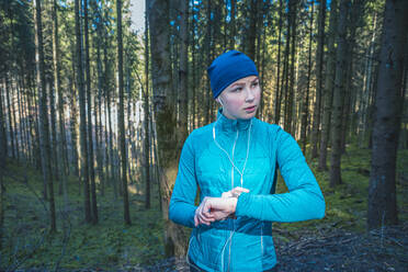 Young female jogger checking the time and looking sideways in the woods - VTF00620