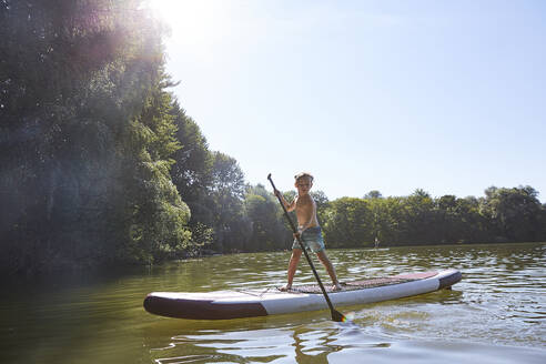 Junge steht auf SUP-Board in der Abenddämmerung - AUF00320