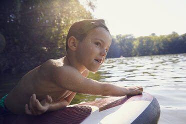 Wet boy climbing on SUP board at evening twilight - AUF00324