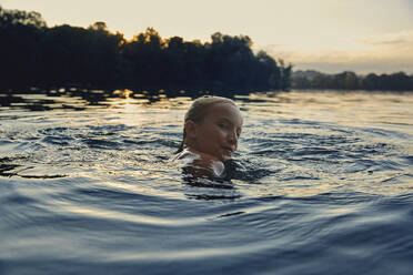 Girl swimming in a lake at evening twilight - AUF00325