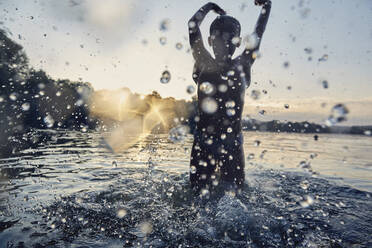 Silhouette eines Mädchens, das bei Sonnenuntergang in einem See plantscht - AUF00327