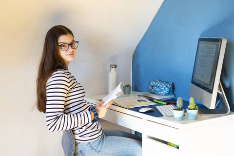 Porträt eines Schulmädchens, das zu Hause am Schreibtisch sitzt und Hausaufgaben macht, lizenzfreies Stockfoto