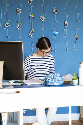 Porträt eines Mädchens, das zu Hause am Schreibtisch sitzt und Hausaufgaben macht, lizenzfreies Stockfoto