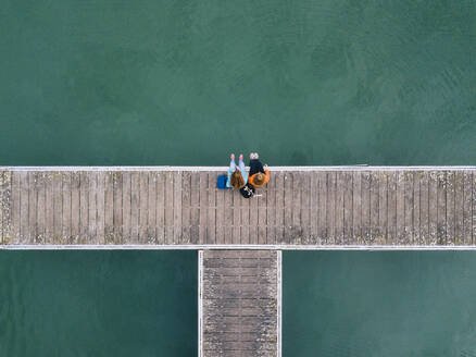 Two friends sitting side by side on jetty, Valdemurio Reservoir, Asturias, Spain - DGOF00651