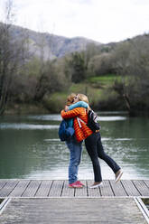Zwei glückliche Frauen mit Rucksäcken stehen auf einem Steg und umarmen sich, Stausee Valdemurio, Asturien, Spanien - DGOF00663