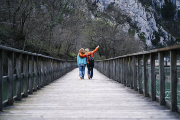 Rückenansicht von zwei besten Freunden, die Seite an Seite auf der Uferpromenade spazieren gehen, Stausee Valdemurio, Asturien, Spanien - DGOF00665