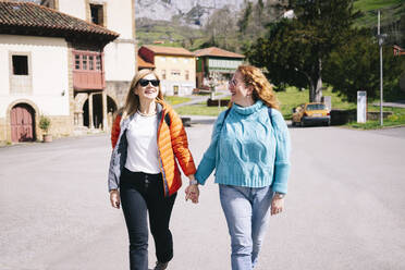 Zwei glückliche Frauen mit Rucksäcken, die Hand in Hand spazieren gehen, Stausee Valdemurio, Asturien, Spanien - DGOF00675